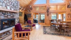 L’intérieur d’une cabane en rondins, avec une cheminée en pierre, des meubles en bois et des têtes de cerf accrochées au mur.