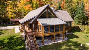 Une cabane en bois dotée d’une grande terrasse, d’un porche couvert et d’un escalier menant à l’étage principal.