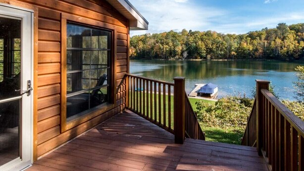 Une cabane en bois dotée d’une terrasse donnant sur un lac, entourée d’arbres.