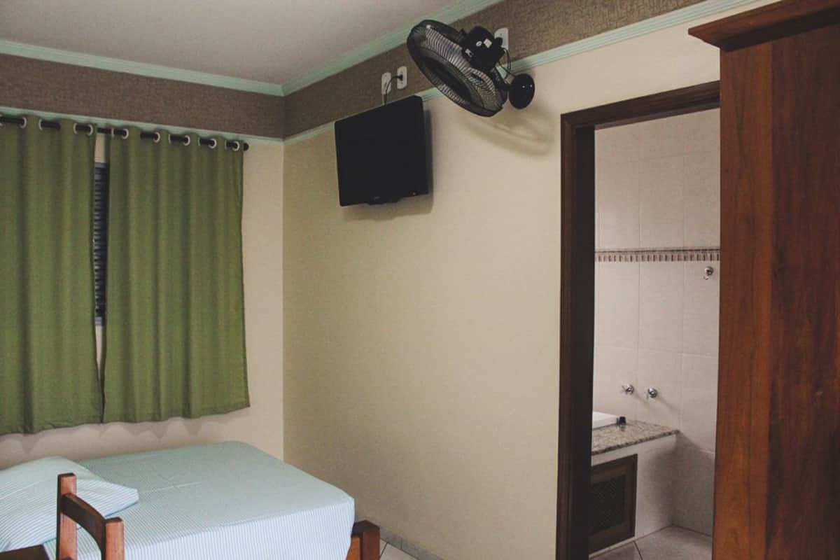 A room with a bed, a television mounted on the wall, and a bathroom visible through an open door.