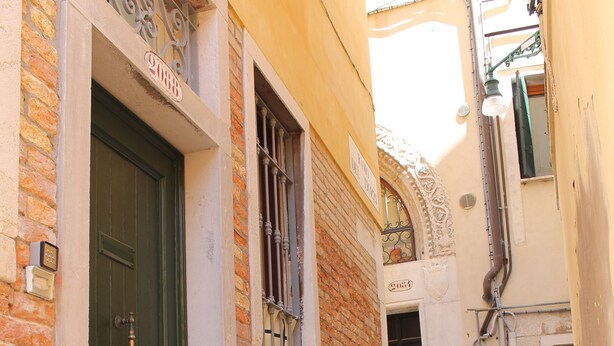 Un callejón estrecho con una puerta verde y una ventana con barrotes.