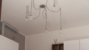 Una cocina moderna con armarios blancos, una mesa de comedor de madera y sillas blancas. Un candelabro con varias lámparas cuelga sobre la mesa.