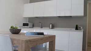 Una cocina moderna con armarios blancos, un microondas, un hervidor y una tableta sobre una mesa de madera.