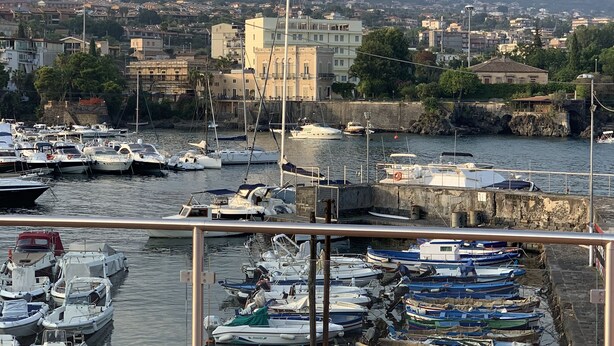 Un port de plaisance où sont amarrés différents types de bateaux, avec une vue sur la ville en arrière-plan et un ciel dégagé.