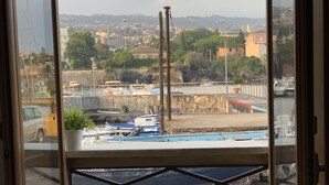 Vue depuis une pièce dotée d’une grande fenêtre donnant sur un port, avec des bateaux, un quai et une vue lointaine sur la ville.