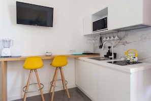 A modern kitchen with a flat-screen TV, a microwave, a sink, and two yellow bar stools.