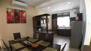 A dining area with a dark wooden table and chairs, a kitchen with dark cabinets and a refrigerator, and a window with curtains. - Luxury Villa with privet outdoor swiming pool. (Kundasale)