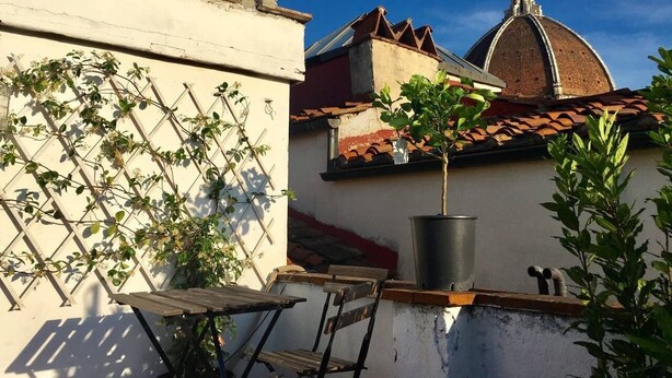 A courtyard with a wooden table and chairs, a potted plant, and a building with a dome and tiled roof. - Duomo View Rooftop Terrace - Bright & Quiet 3 Bedroom 2 Bath (Firenze)