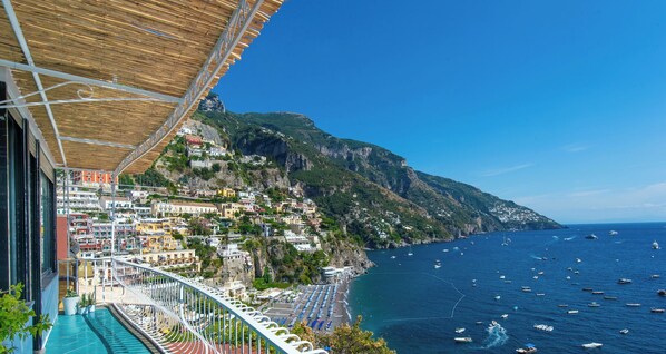 A balcony with a view of a coastal town, a clear blue sky, and the sea with boats.