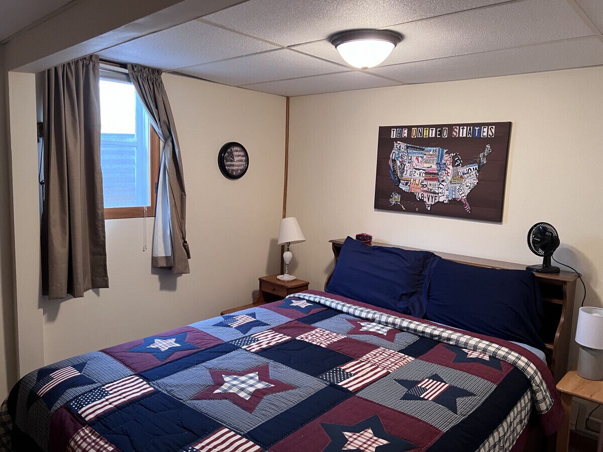A bedroom with a large bed, a wall clock, a map of the United States, and a window with curtains.
