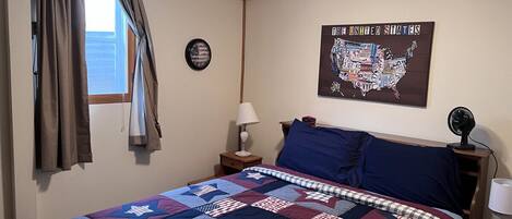 A bedroom with a large bed, a wall clock, a map of the United States, and a window with curtains.