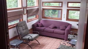 A room with a purple sofa, a chair, and a small table. There are windows with blinds and a view of greenery outside. - Hideout On Lake Delton ( Known as the Getaway ) (Lake Delton)