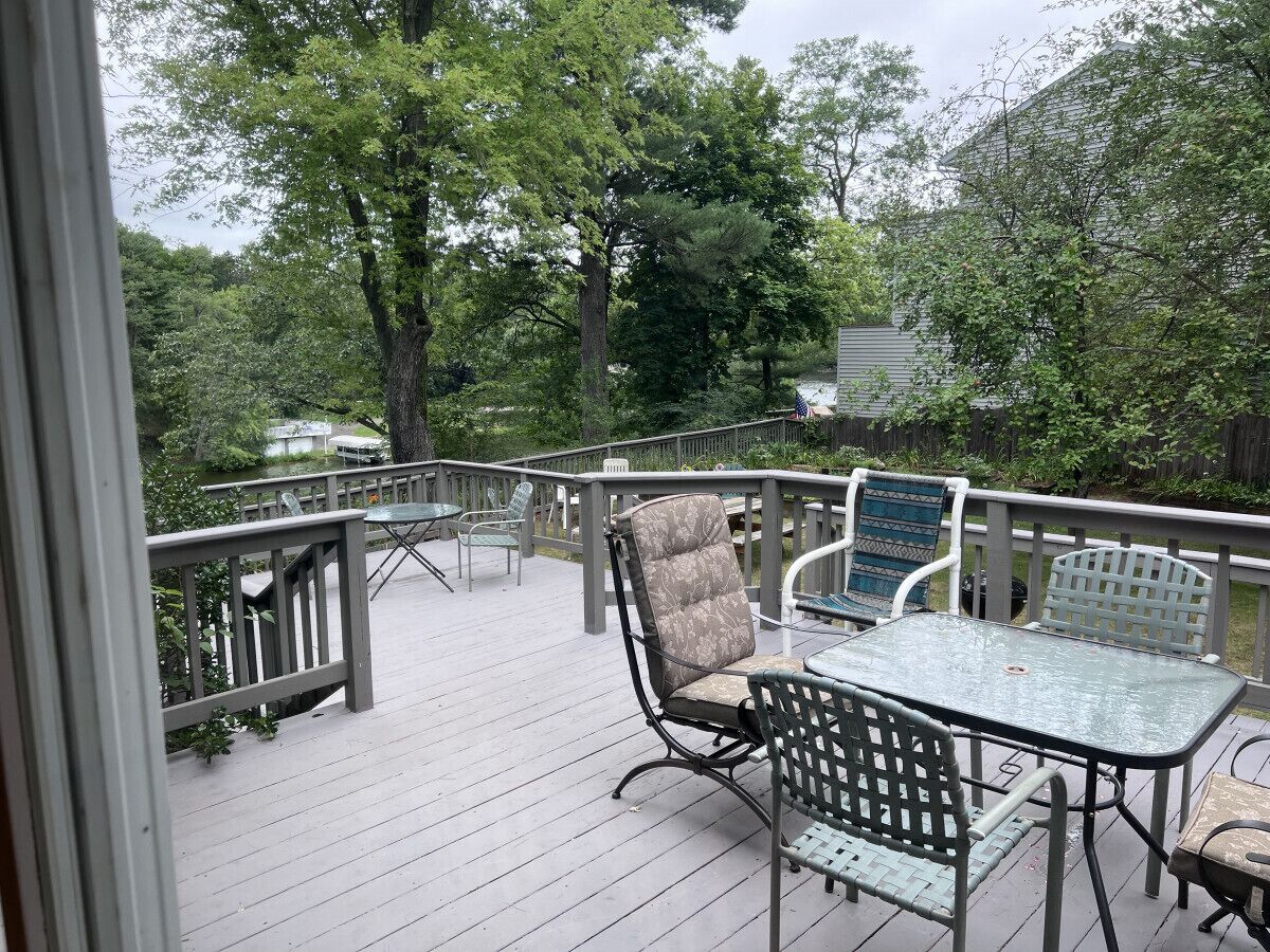 An outdoor deck with a table and chairs, surrounded by a wooden railing and trees.