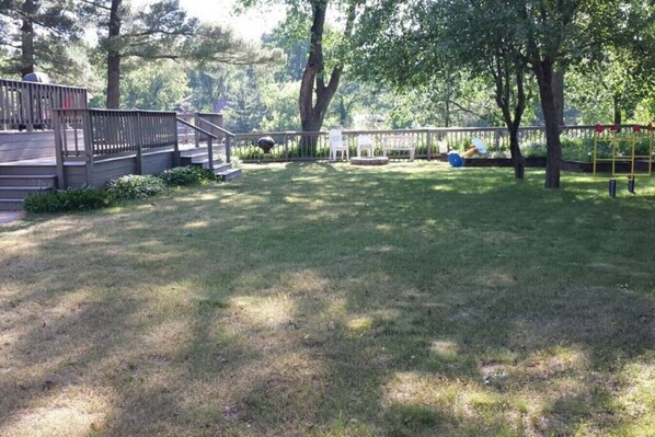 A grassy outdoor area with a wooden deck, steps leading up to a covered area, and a playground with a yellow swing set. - Hideout On Lake Delton ( Known as the Getaway ) (Lake Delton)
