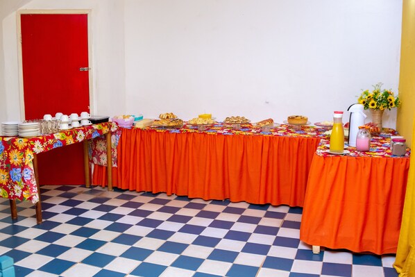 Una habitación con suelo a cuadros, una puerta roja y una mesa con mantel floral y mantel naranja.
