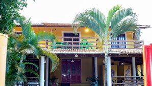 A two-story building with a balcony, outdoor seating, and potted plants. - Pousada Pêlo De Imbassai (Mata de São João)