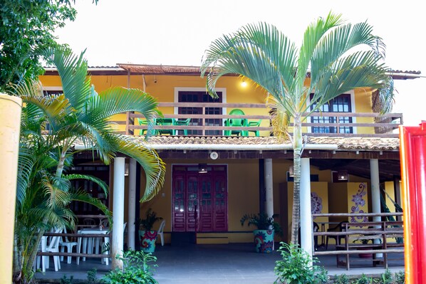 A two-story building with a balcony, outdoor seating, and potted plants. - Pousada Pêlo De Imbassai (Mata de São João)