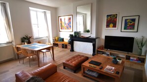 Ein helles Wohnzimmer mit Kamin, Fernseher und Essbereich mit Tisch und Stühlen.