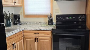 Une cuisine compacte avec des meubles de rangement en bois, une cuisinière noire, un four à micro-ondes et une machine à café.