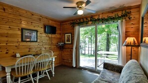 L’intérieur chaleureux d’un chalet comprend une table à manger, des chaises, un canapé, un ventilateur de plafond et une grande fenêtre donnant sur le paysage extérieur.