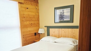 Une chambre avec un lit simple, une tête de lit en bois, un tableau encadré au mur et une fenêtre avec des stores.