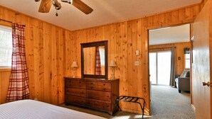 Slaapkamer met houten lambrisering, een bed, een dressoir en een plafondventilator.