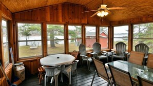 Een houten chalet met een eethoek, grote ramen en een plafondventilator.