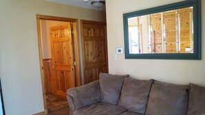 Una habitación con puerta de madera, un sofá gris y una ventana con persianas de madera.