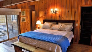 Ein Schlafzimmer mit Holzwandverkleidung, einem Bett, einer Bank, einer Lampe und einer Schiebetür aus Glas.