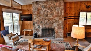 Ein gemütliches Wohnzimmer mit Kamin aus Stein, Holzwänden, einer bequemen Couch und einem Fernseher.