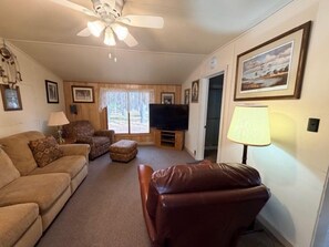 A living room with a sofa, armchair, ottoman, TV, and a ceiling fan.