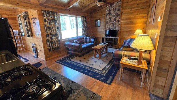 Un interior acogedor de cabaña con chimenea, un sofá, un televisor y un comedor.