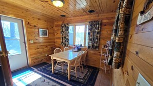 Interior de una cabaña de madera con una mesa de comedor, sillas, una ventana, cortinas, una puerta y un letrero que dice 'UP-North'.