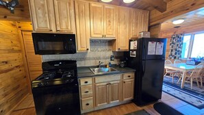 Cocina de cabaña de madera con estufa, microondas, refrigerador y armarios de madera.