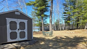Una caseta con puerta y ventanas blancas, una mesa de picnic y un patio con césped y árboles.