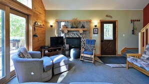 A cozy living room with a fireplace, a television, and comfortable seating. - Deer Trail Log Home #13  on Lake Delta near Iron River, WI (Iron River)