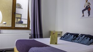 Ein Hotelzimmer mit Bett, Heizkörper, Fenster mit Vorhängen und einem Poster an der Wand.