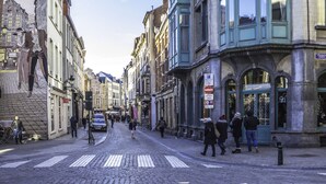 Eine Kopfsteinpflasterstraße gesäumt von historischen Gebäuden, eine Fußgängerampel und Passanten.
