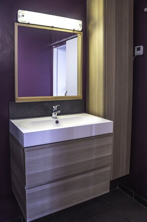 Een badkamer met een witte wastafel, een spiegel met gouden lijst en een houten kastje eronder.