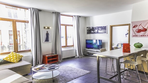 Ein modernes Wohnzimmer mit einer Couch, einem Couchtisch mit Zeitschriften, einem Fernseher und einem Essbereich mit Stühlen.