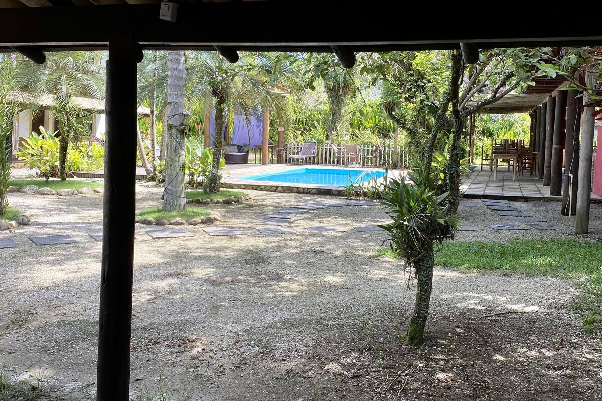 A covered outdoor area with a pool, surrounded by greenery and a wooden deck.