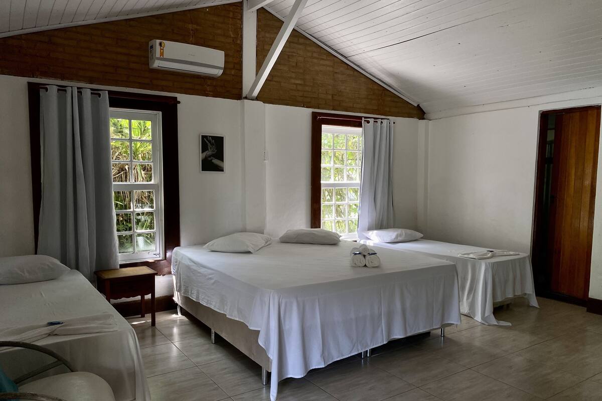 A room with two single beds, a wooden ceiling, and a window with a view of greenery.