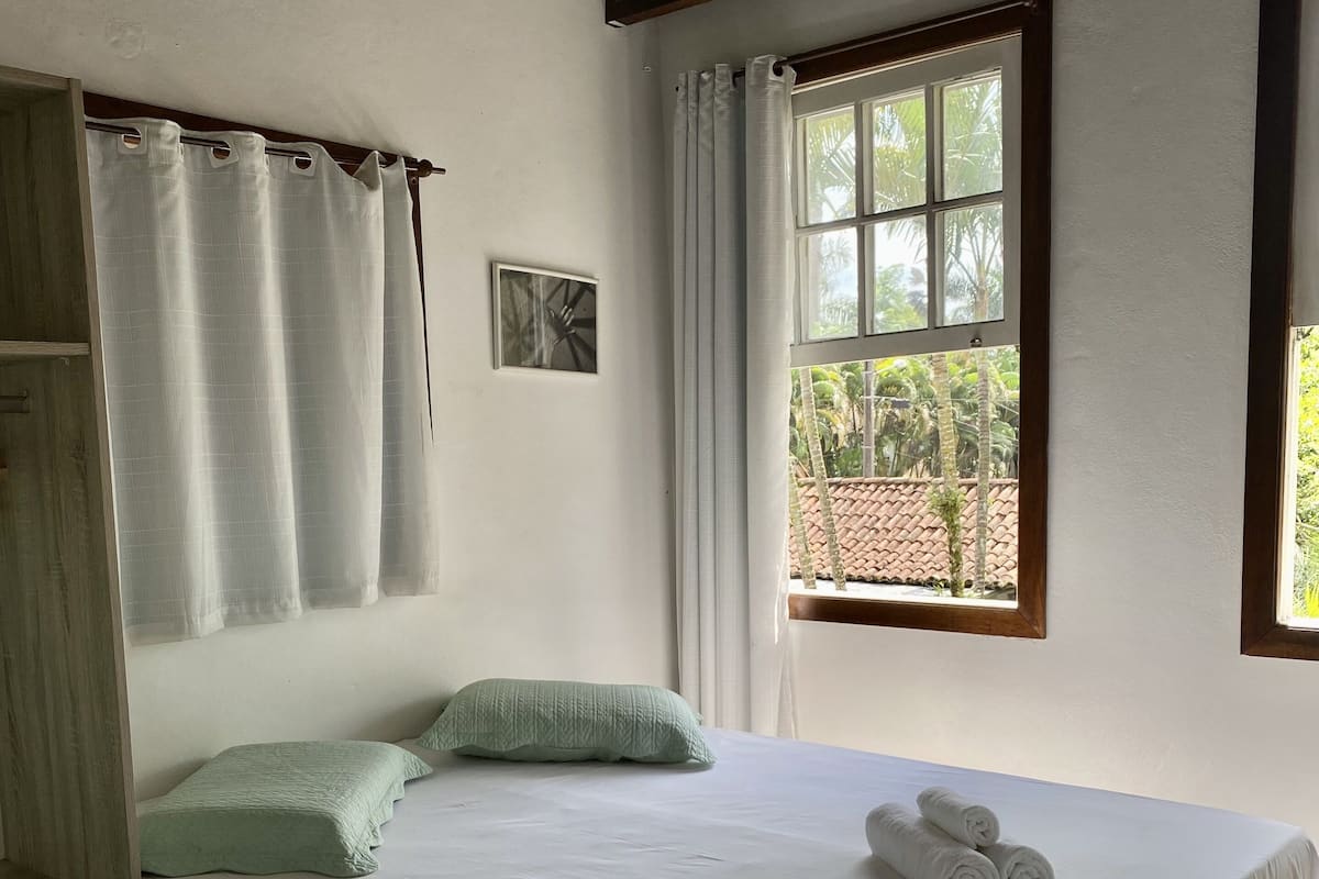 A single bed with a white sheet, two green pillows, and a rolled towel on the side.