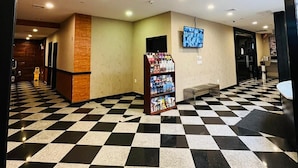 Un hall con suelo a cuadros, una recepción, un televisor montado en la pared y un revistero.