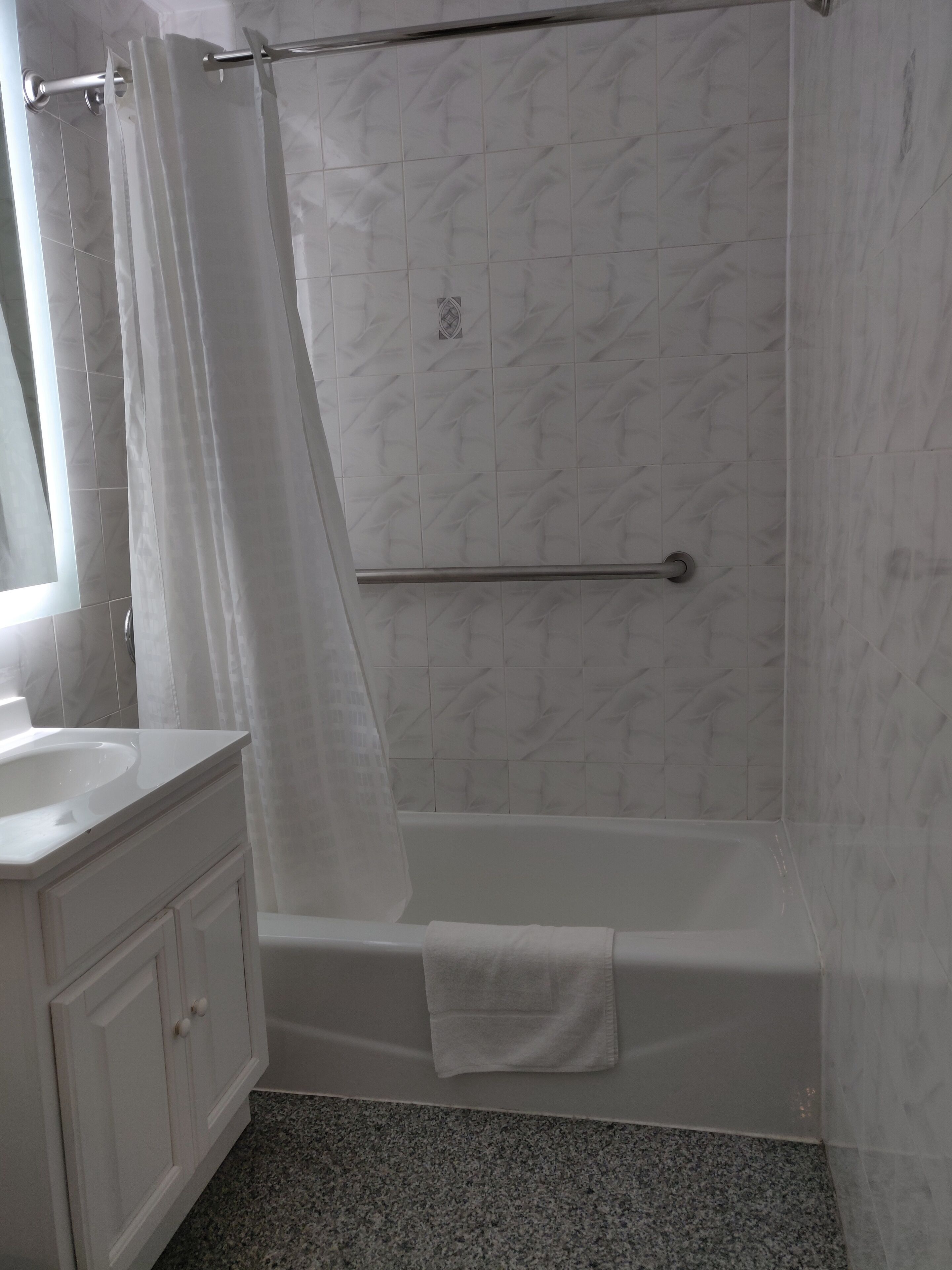 Un baño con una bañera blanca, cortina de ducha, toalla y tocador con espejo.