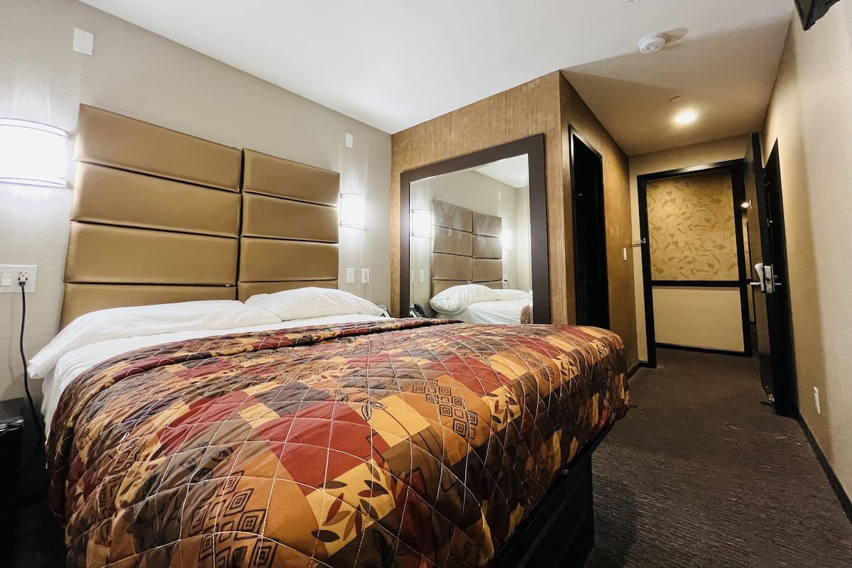A hotel room with a large bed, a headboard, a mirror, and a door leading to another room.