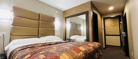 A hotel room with a large bed, a headboard, a mirror, and a door leading to another room.