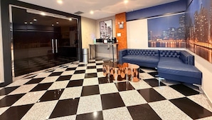 Un vestíbulo de hotel con piso a cuadros, un sofá azul, una estación de café y un mural con vista a la ciudad.