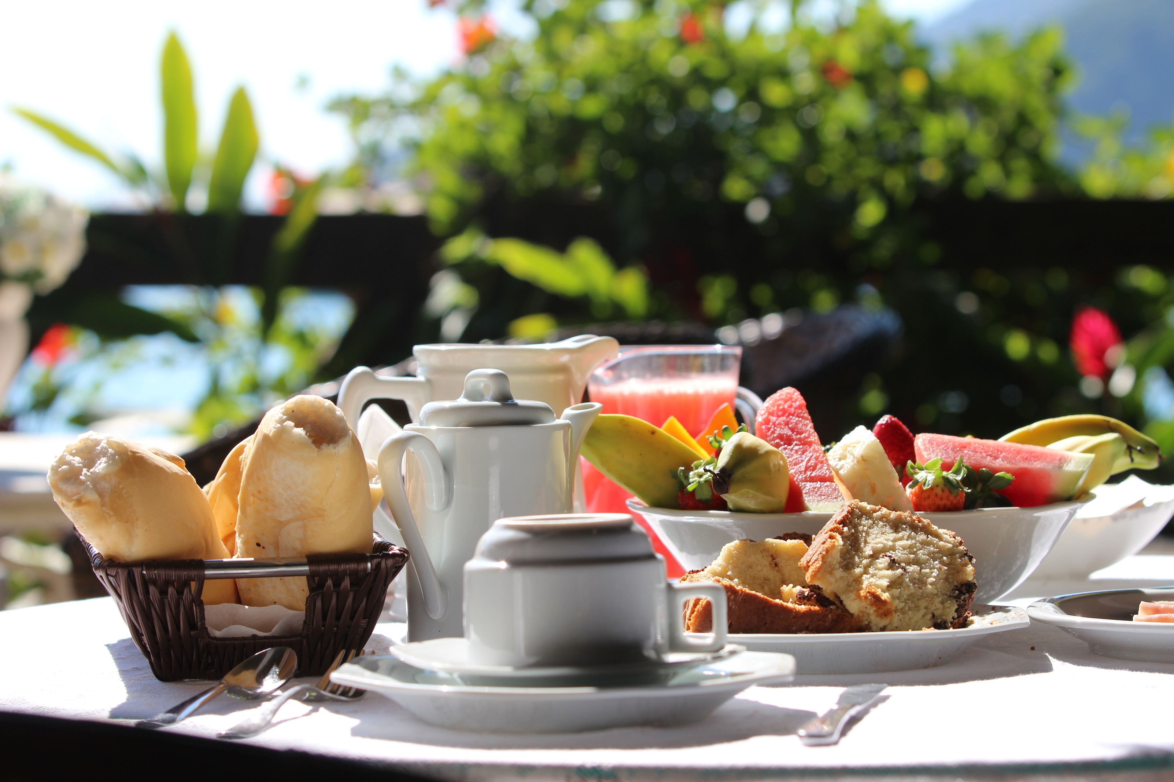 A table set with breakfast items including bread, a teapot, cups, and a bowl of fruit.