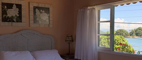 A bedroom with a bed, a nightstand, a lamp, and a window with a view of greenery and water.
